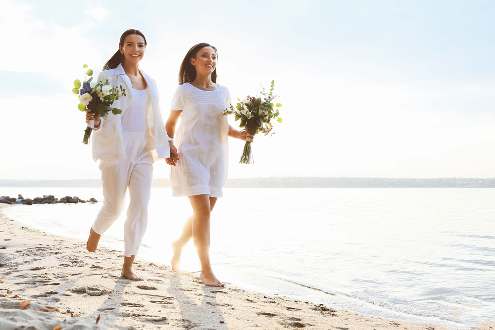 Beautiful lesbian couple walking along a river bank on their wedding day